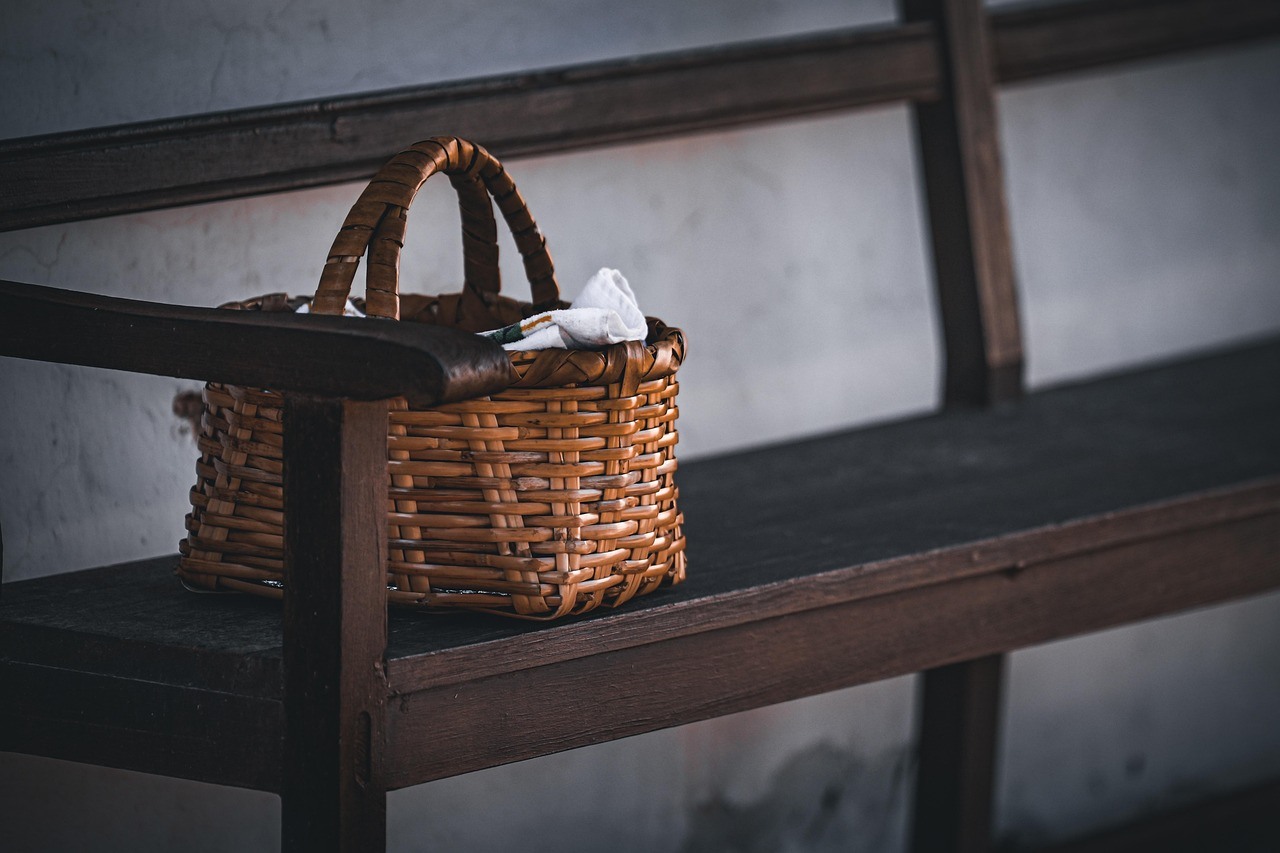 A compact brown basket with looped handles rests on a dark wooden bench.