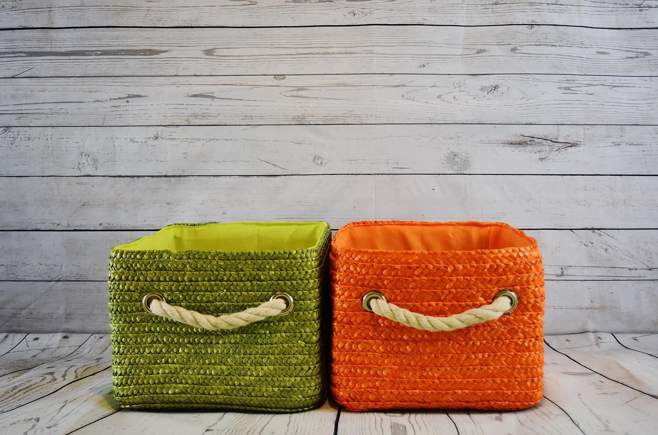 Two square woven storage bins, one green and one orange, stand against whitewashed wooden boards.